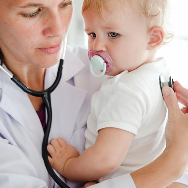 A healthcare professional performs a check-up on a small child, using a stethoscope in a bright, modern medical setting.